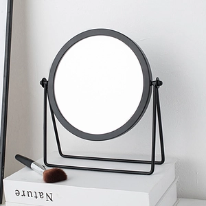 Minimalist round makeup mirror with black frame and metal stand on books