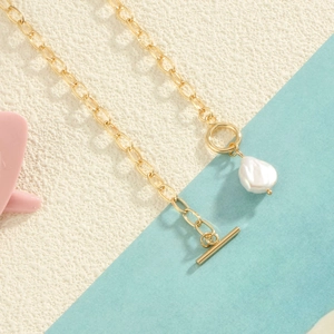 Golden toggle clasp necklace featuring a natural white baroque pearl on stone background