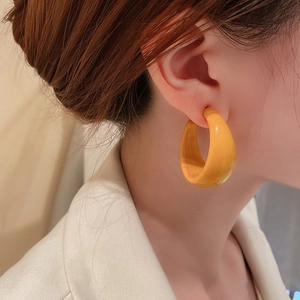 Close-up of model wearing thick yellow C-shaped resin hoop earrings with glossy finish
