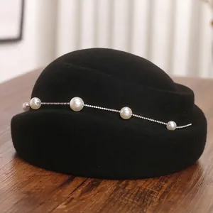 Béret élégant en laine noire avec chaîne de perles et strass sur surface en bois
