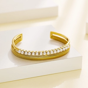 Detail of gold double-layer open bangle with white pearls and chevron textured metal