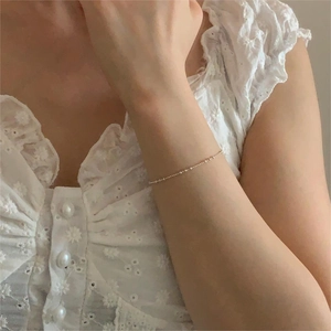 Macro shot of minimalist gold beaded bracelet on model wearing white lace sleeve