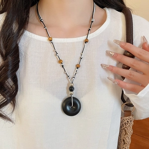 Detail of vintage resin and wood bead pendant necklace on model with woven bag
