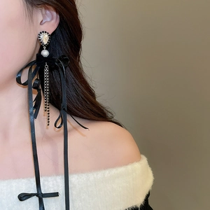 Détail des boucles d'oreilles longues à pompon noir avec nœud en velours et perles
