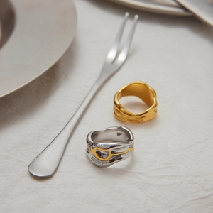 Detail of irregular lava-style rings in gold and silver finish on white textured fabric
