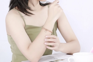 Close-up of a rose gold beaded bracelet with a heart charm on a woman's wrist