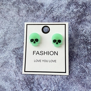 Macro detail of mint green skull stud earrings on a fashion display card