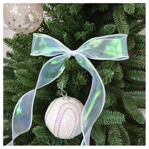 Close-up of a white sequined Christmas ball with iridescent ribbon on a green tree branch