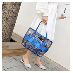 Close-up of blue transparent PVC tote bag held by a model in a minimal outdoor setting