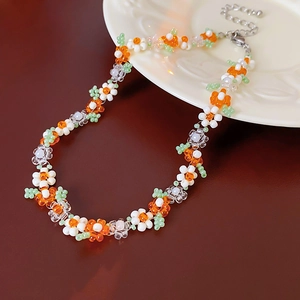 Close-up of handmade beaded floral necklace with white and orange flowers and green leaves