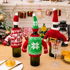 Three knitted Christmas wine bottle covers with reindeer and Santa motifs on a wooden table