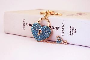 Close-up of heart lock and key keychain with blue rhinestones on a white book