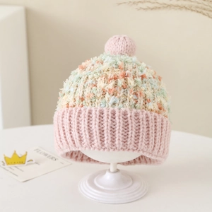 Detail van roze gebreide babymuts met kleurrijke pompon en zachte ribboord
