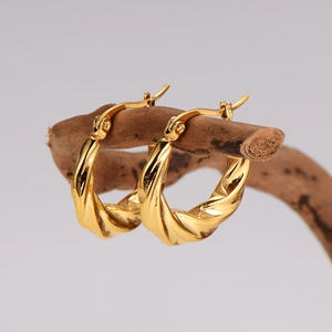 Chic twisted gold earrings displayed on a natural branch against a grey background