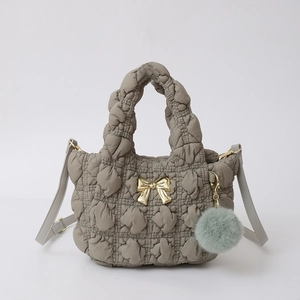 Détail d'un sac en nylon gris matelassé avec nœud doré et pompon en peluche doux