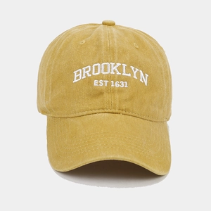 Close-up of white Brooklyn embroidery on a mustard yellow washed vintage baseball cap