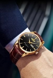 Detail of quartz watch with gold case, black dial, and date display on leather strap