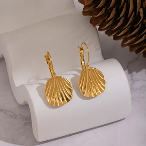 Golden shell-textured earrings in stainless steel on white pedestal with natural decor