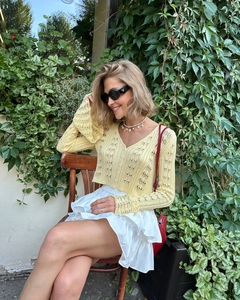 Close-up of light yellow hollow crochet knit cardigan with white buttons and V-neckline