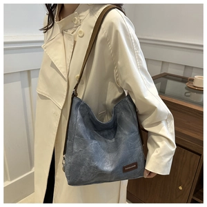 Detail of grey-blue canvas tote bag featuring brown shoulder straps and fashion leather label