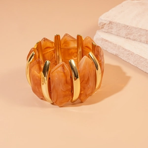 Détails d'un large bracelet en résine avec des facettes ambrées et des maillons en métal doré