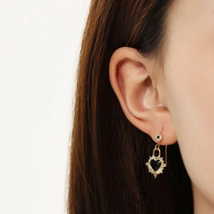 Gros plan d'une boucle d'oreille cœur doré avec centre noir et rayons de soleil