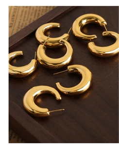 Polished gold plated C-shaped chunky hoop earrings scattered on a vintage wooden tray