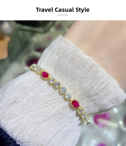 Detail of gold-plated bracelet with oval rubies and round zirconias on a white sleeve