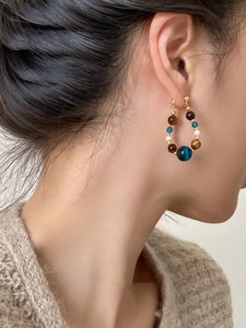 Détail latéral de boucles d'oreilles créoles dorées avec perles et œil de tigre
