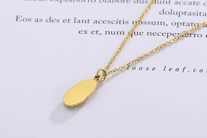 Détail macro du pendentif pièce ovale dorée avec finition mate sur une fine chaîne dorée