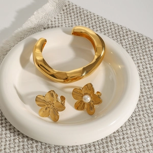 Detail of gold floral rings with white pearl and irregular open cuff bracelet on a ceramic tray
