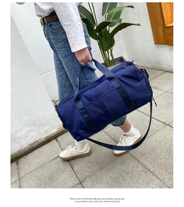Blue nylon travel bag with gold hardware and shoulder strap shown in a lifestyle street setting