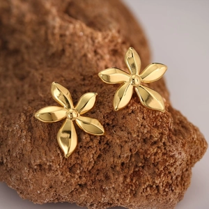 Macro shot of gold five-petal flower earrings on a textured natural stone background
