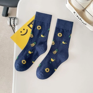 Navy blue cotton crew socks featuring yellow pineapple and drink patterns on a white desk