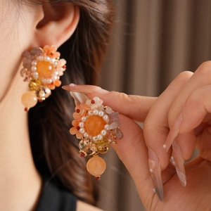 Détail de boucles d'oreilles vintage avec perles et pierres oranges portées par un mannequin