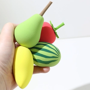 Hand holding fruit-shaped makeup sponges including strawberry and lemon beauty blenders
