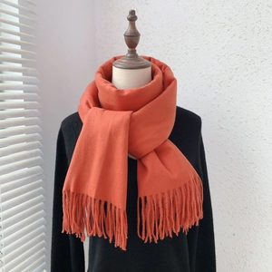 Detail shot of a soft orange cashmere-feel scarf with fringe on a female model