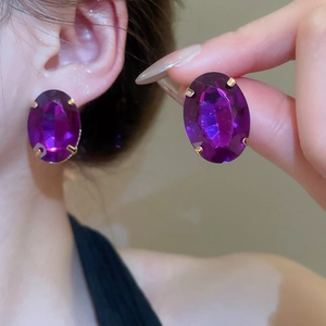 Macro shot of oval purple crystal earrings with gold prong setting on model ear