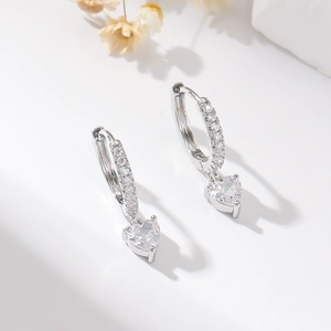 Silver hoop earrings with heart-shaped zircon pendants on a minimalist white background