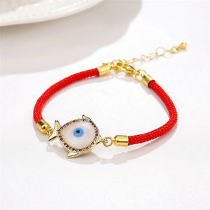 Macro view of adjustable red woven bracelet featuring a gold fish evil eye pendant