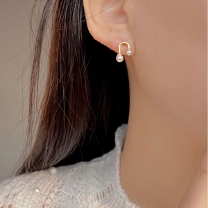 Detailed view of elegant U-shaped gold earrings with pearls worn by a model