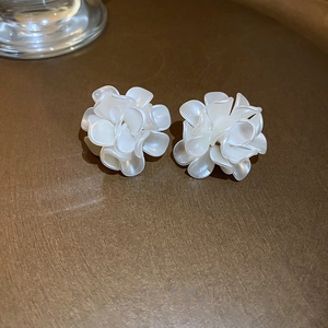 Elegant white acrylic flower stud earrings with silver needles on a dark metal tray