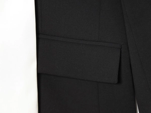 Détail de la veste noire montrant la texture sergée et la finition de la poche à rabat
