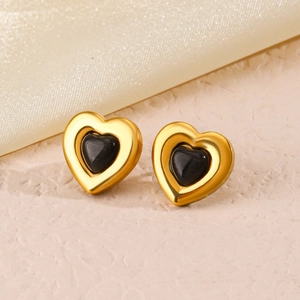 Golden heart earrings set with black gemstone centers on minimalist textured surface