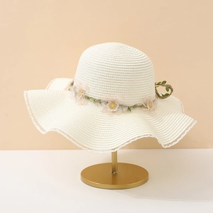 Détail d'un chapeau de paille à large bord orné de fleurs en tissu et d'une vigne