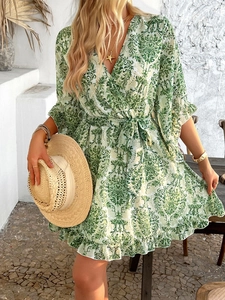 Detail of green floral wrap dress with V-neck and waist tie featuring a straw hat accessory