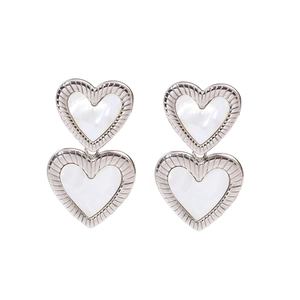 Détail de boucles d'oreilles double cœur argentées avec incrustation en nacre blanche