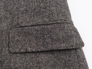 Detailed close-up of brown herringbone wool fabric and precise stitching on the jacket