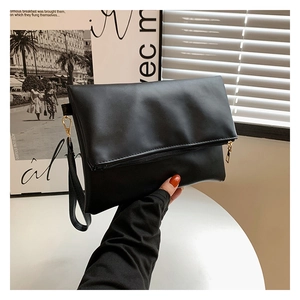 Dettaglio della pochette a busta minimalista in pelle nera opaca con cinturino