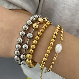 Stacked stainless steel beaded bracelets in gold and silver tones with a pearl accent